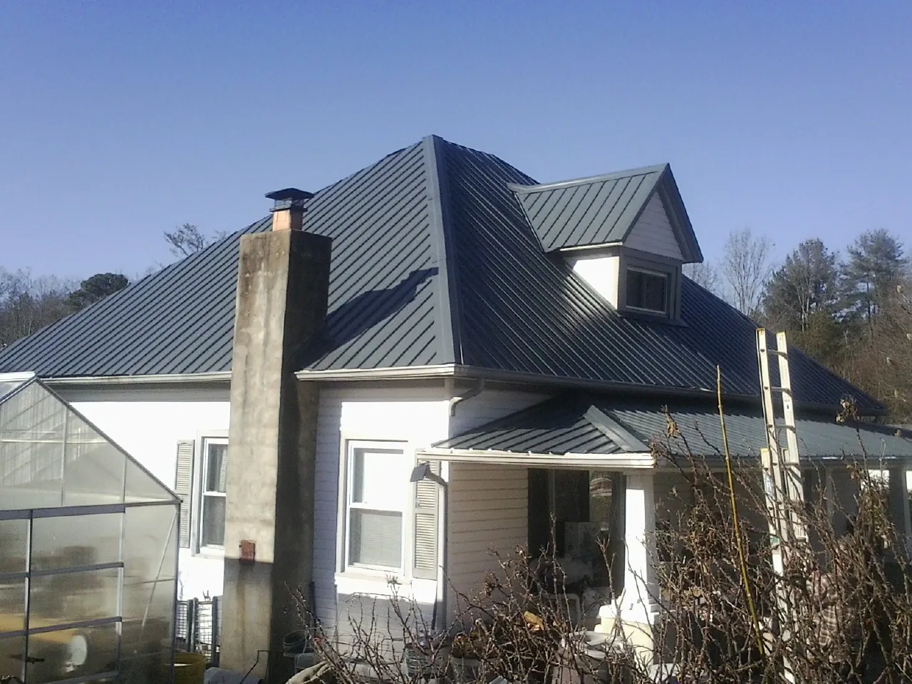 Dark blue standing seam metal roof on a white farmhouse with dormer — Slate & Tile Roof Repair by Roofing Brothers in Poca