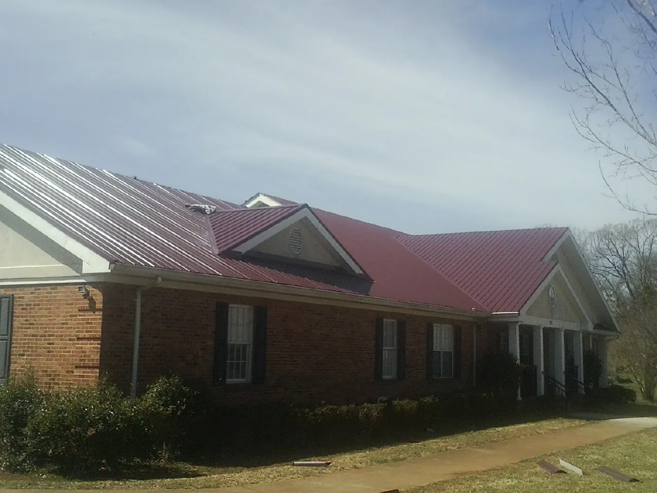 Red metal roof with gabled entries on a long brick building, from a Hail Damage Roof Repair job in Poca
