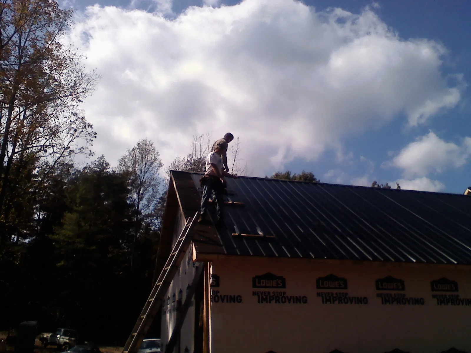 Roofer fastening dark metal panels high against a cloudy sky, from a Roof Inspection job in Poca