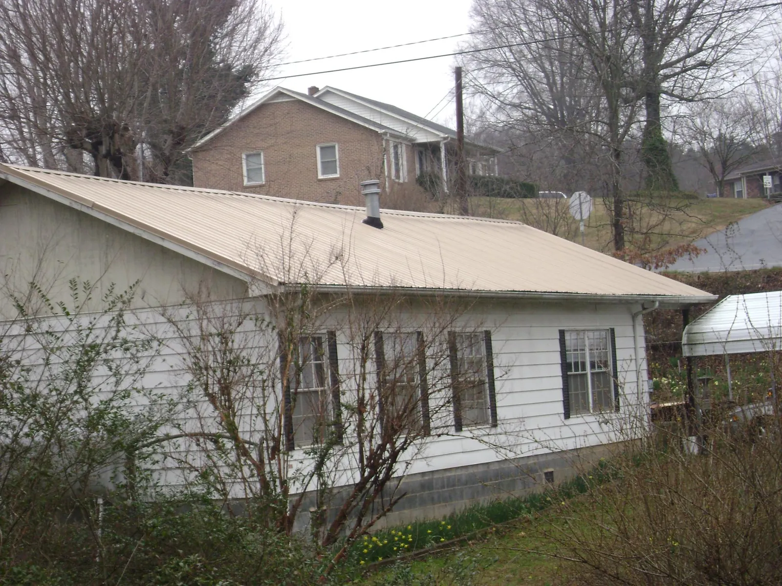 Tan metal roof on a white sided house set into a hillside — Commercial Roofing by Roofing Brothers in Poca