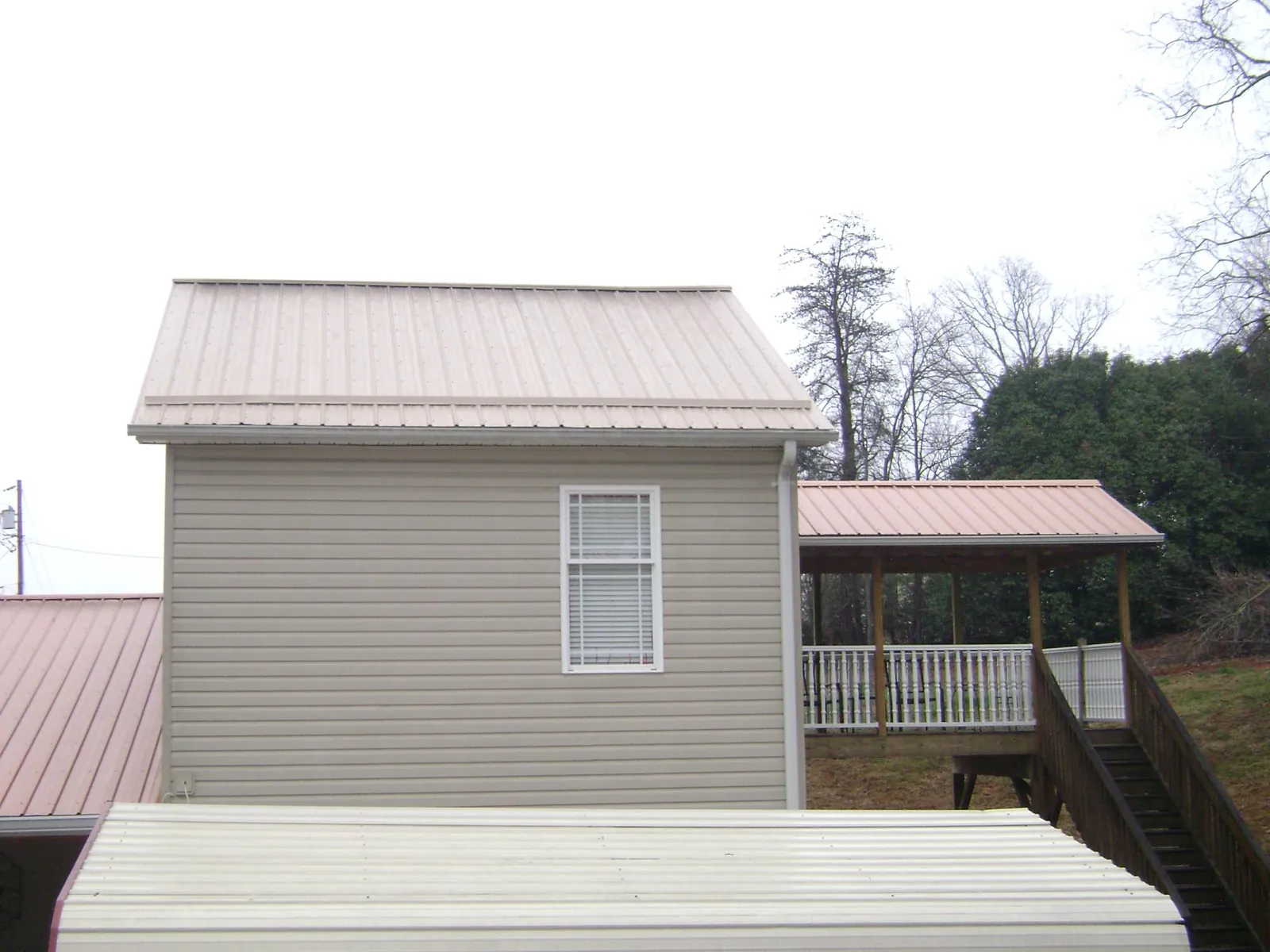 Tan metal roofs on a two story addition and attached porch, from a Roof Replacement job in Poca